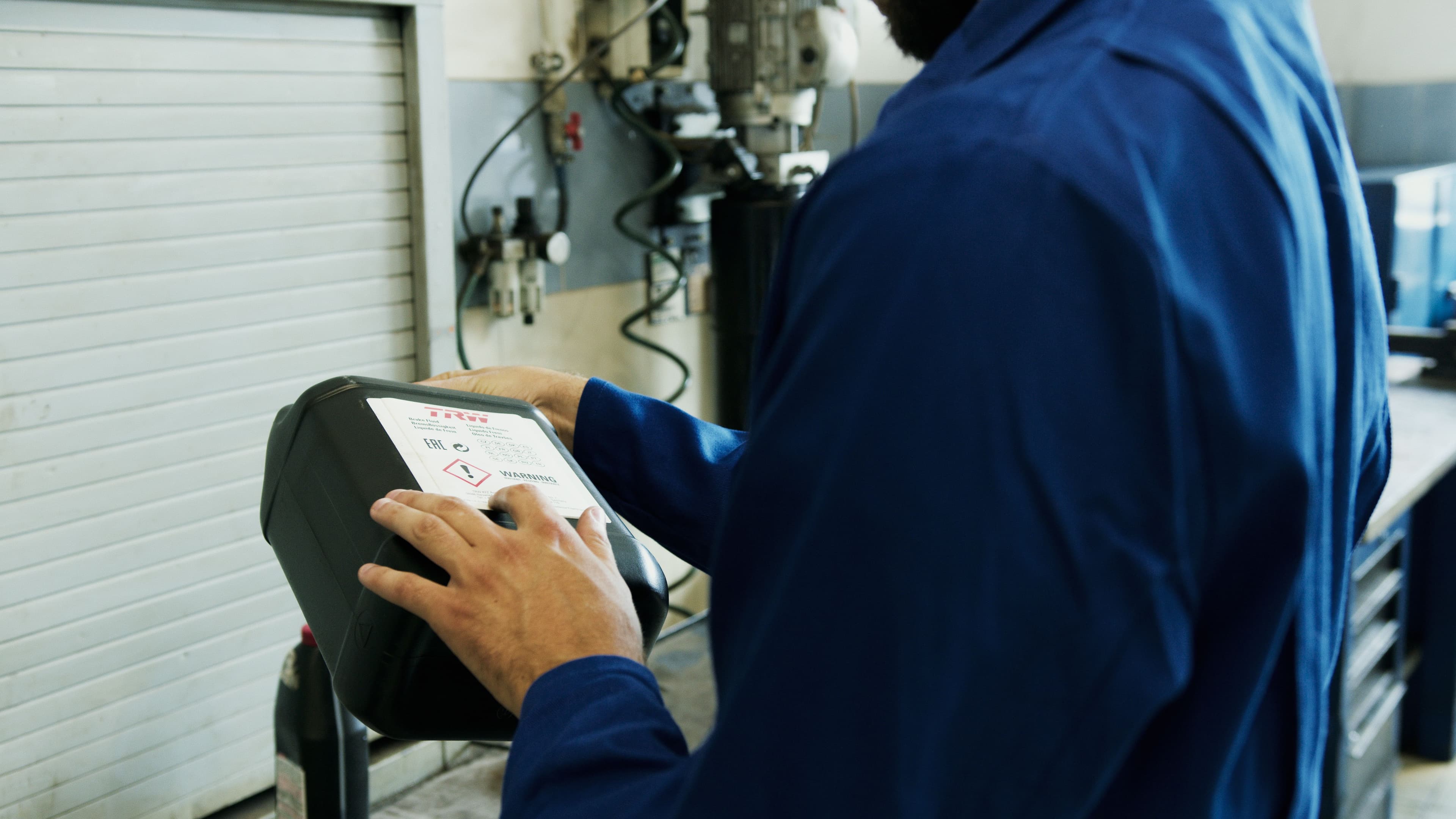 Technician using a diagnostic scan tool beside a vehicle in an automotive workshop