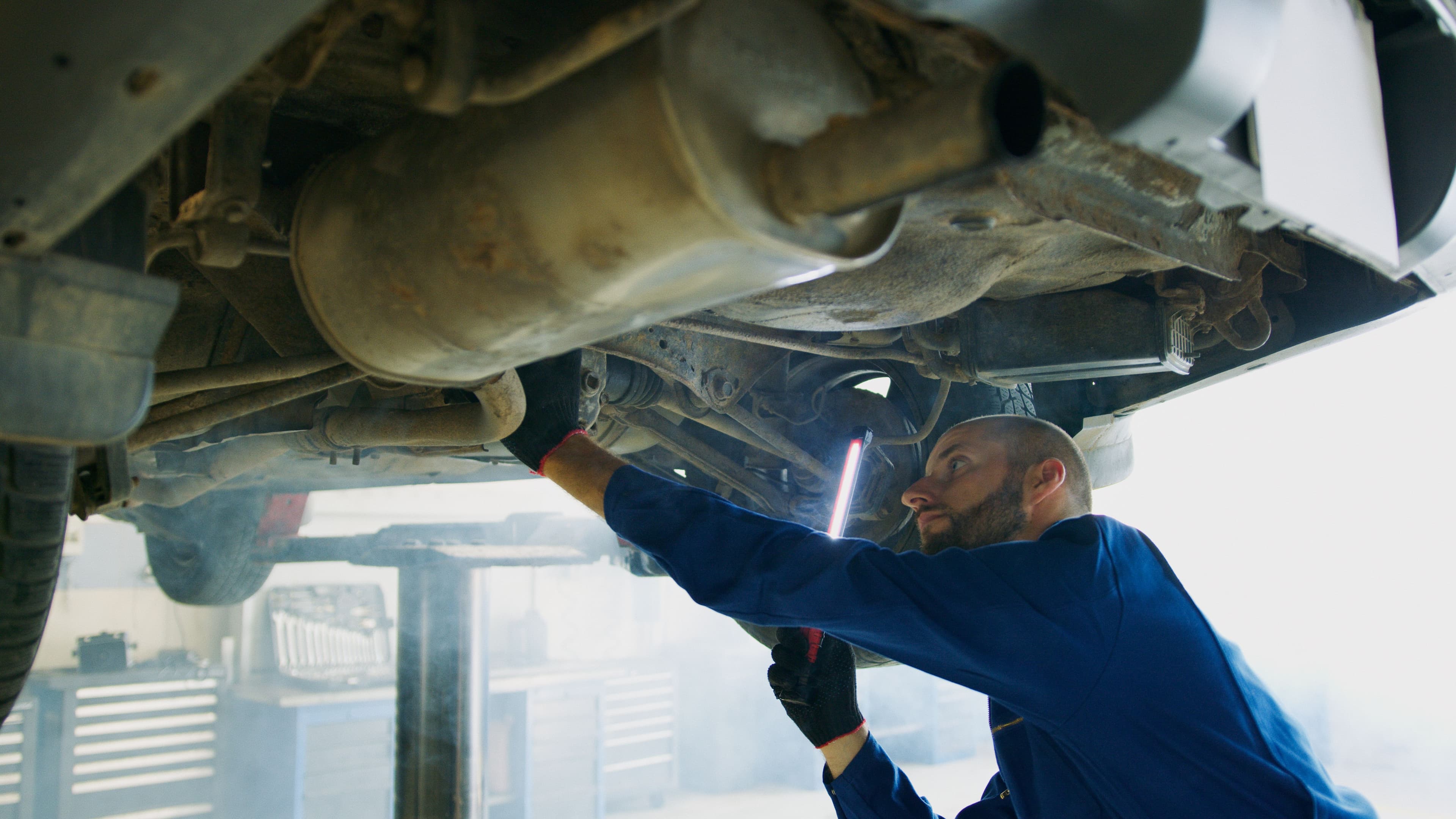 Mechanic inspecting a vehicle undercarriage on a workshop lift
